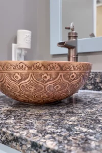 A sink bowl with an ornate design above a fancy cabinet in a bathroom.